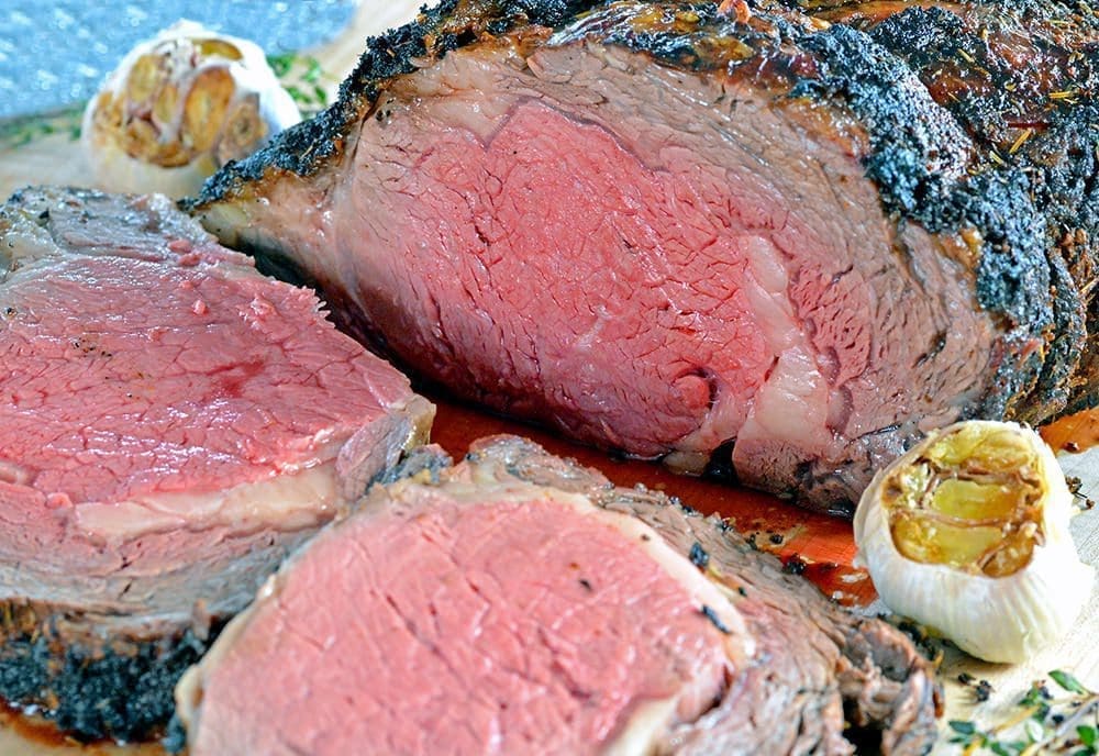 Cooked Prime Rib Recipe - with two slices of pink prime rib and roasted garlic next to it.