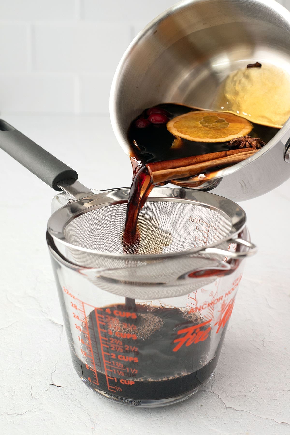 Saucepan of warm red wine being poured through a sieve.