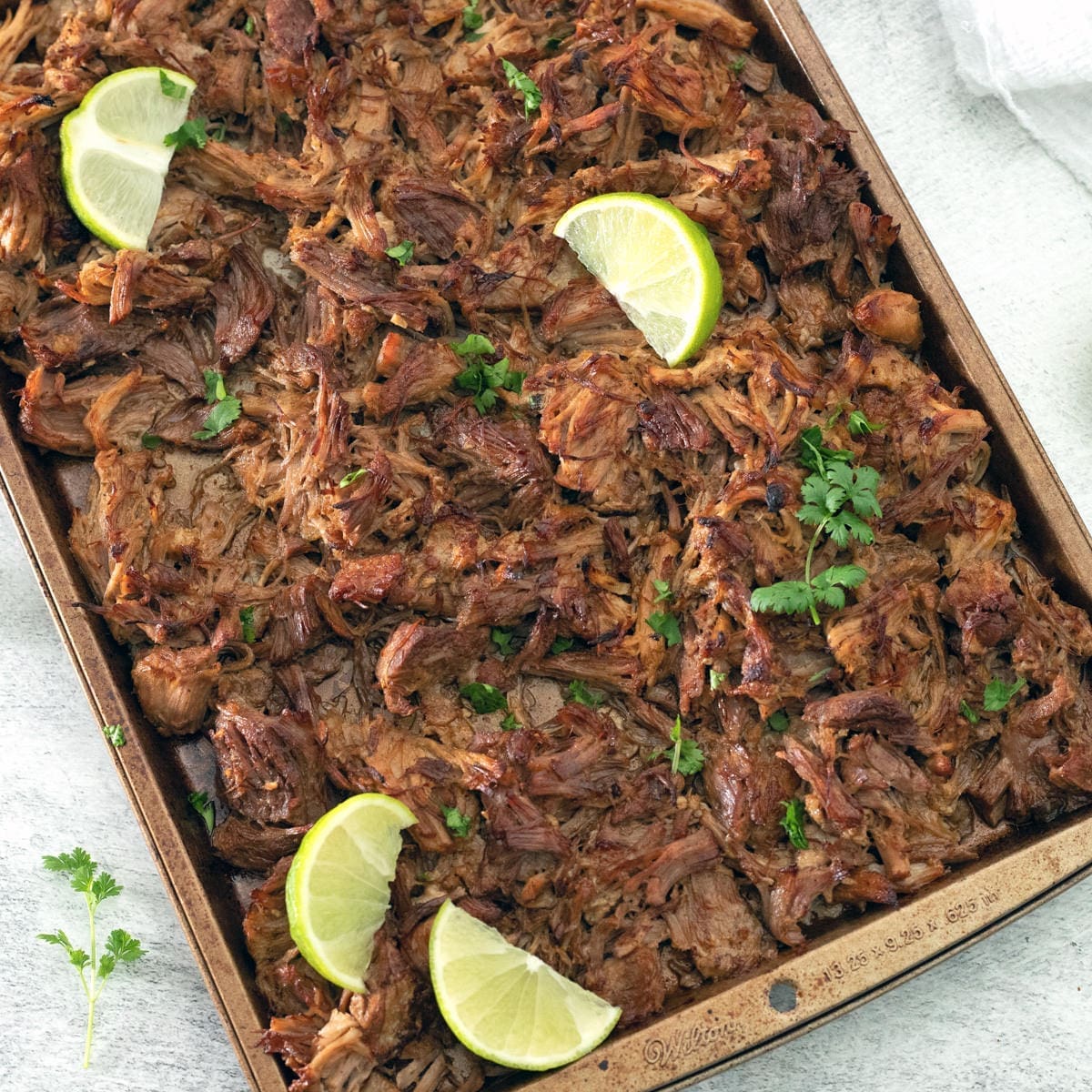 Authentic Carnitas on a baking sheet with lime wedges.