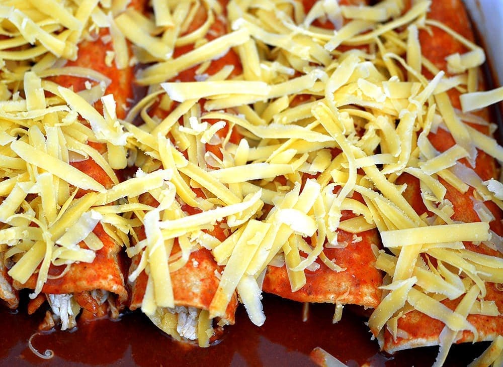 Uncooked chicken enchiladas with cheese on top. 