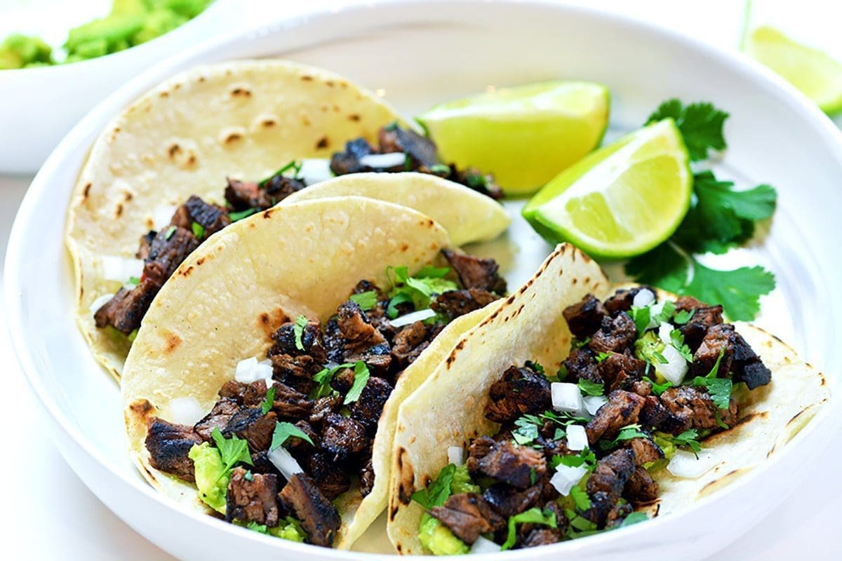 Three topped with cilantro and onions on a white plate. Served with lime slices and cilantro.