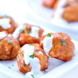 Buffalo chicken meatballs coated in ranch on a white plate.