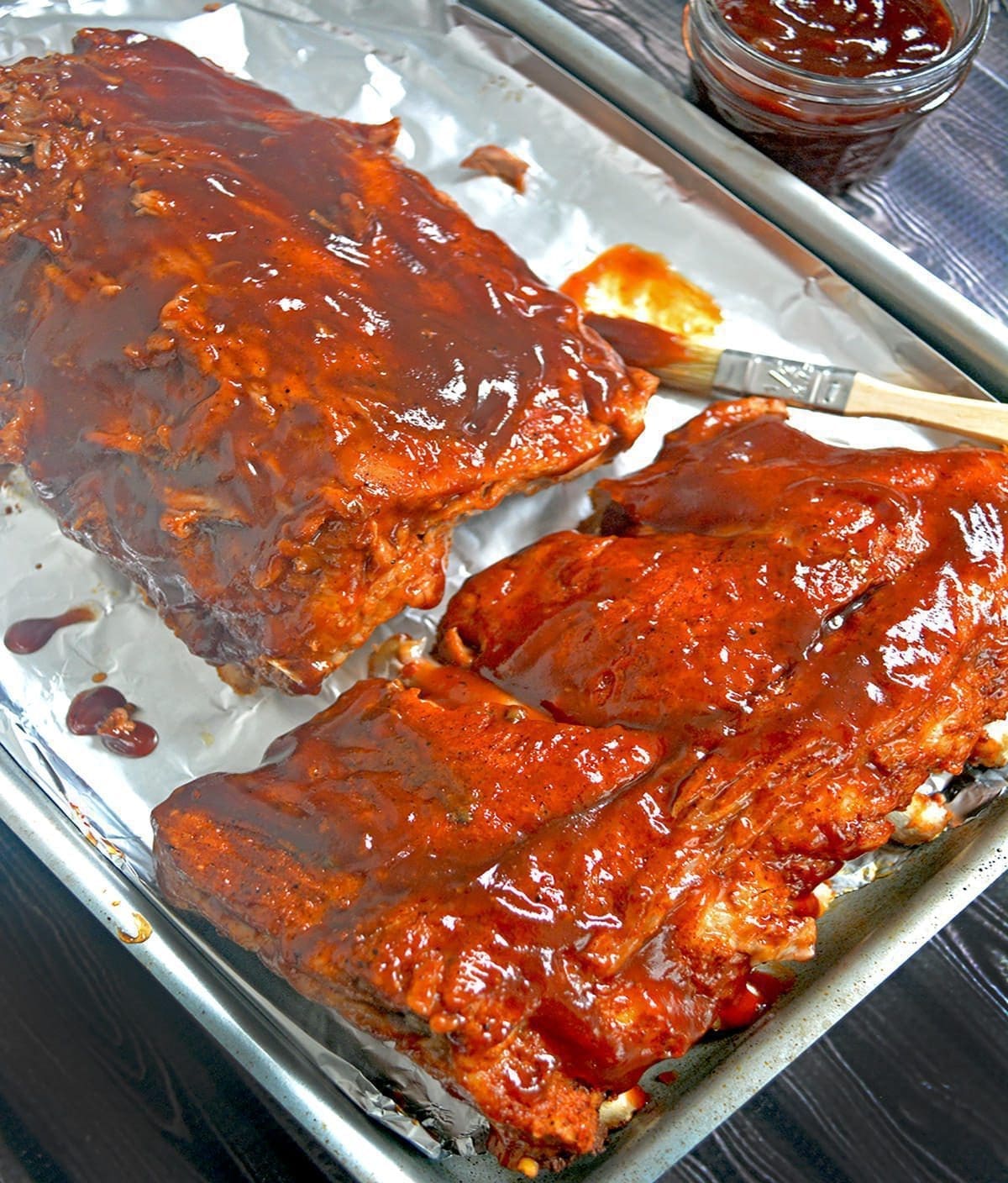 Two slabs of cooked ribs slathered in BBQ Sauce on a cookie sheet.