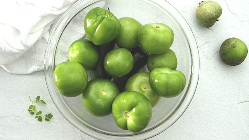 Clear bowl full of husked tomatillos.