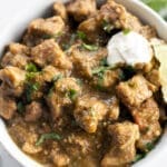 Bowl of green chile verde topped with sour cream and lime wedge.
