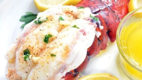 Lobster tail with lemon slices on a white plate.