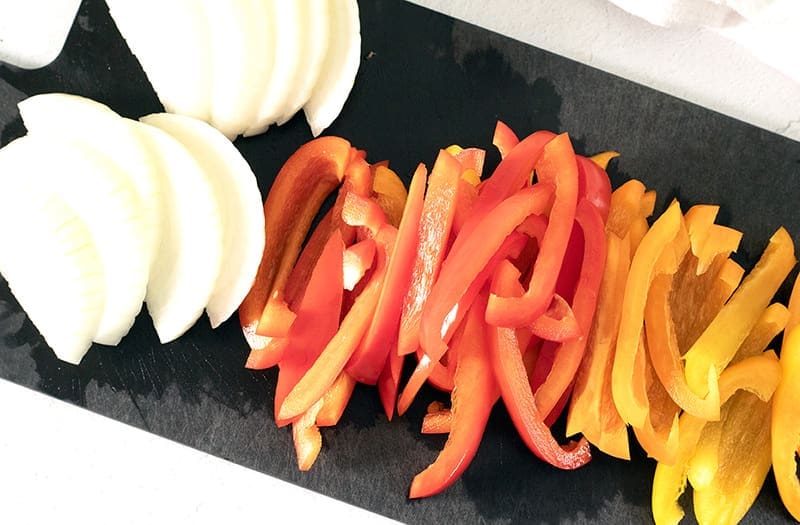 Cut peppers and onions on a black cutting board.