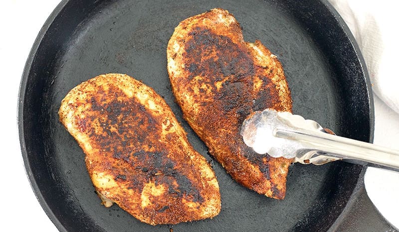 Two cooked chicken breasts in a cast iron skillet.