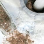 Jerk seasoning in a clear spice jar spilled on white marble. Also shows the seasoning in a mortal and pestal.