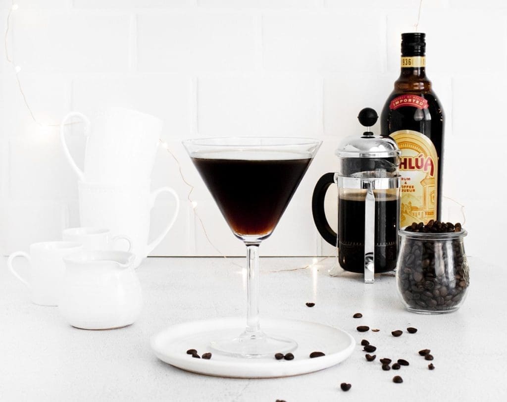 Hazelnut Espresso Martini in a martini glass on a white plater. A bottle of Kahlua and coffee press are in the background;