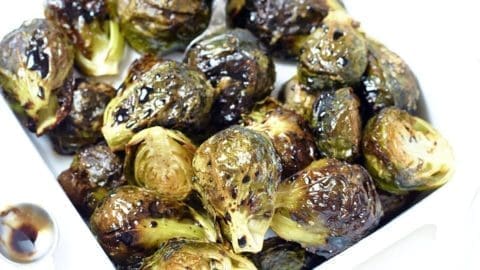 Balsamic Glazed Brussel Sprouts in a white bowl with a silver measuring spoon next to it.