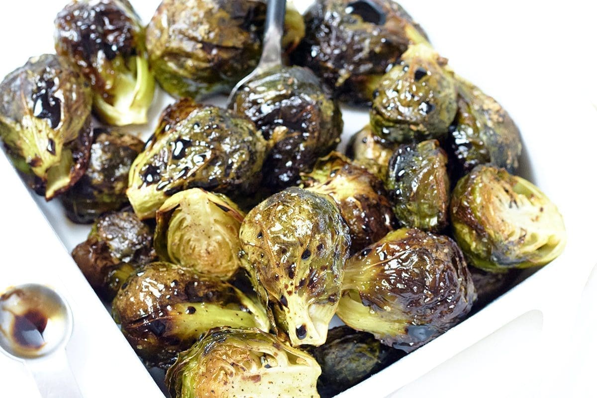 Balsamic Glazed Brussel Sprouts in a white bowl with a silver measuring spoon next to it.