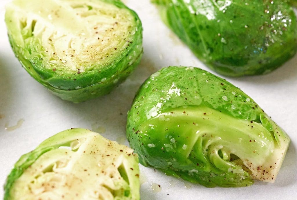Picture of raw halved Brussels sprouts covered in olive oil and pepper and salt.