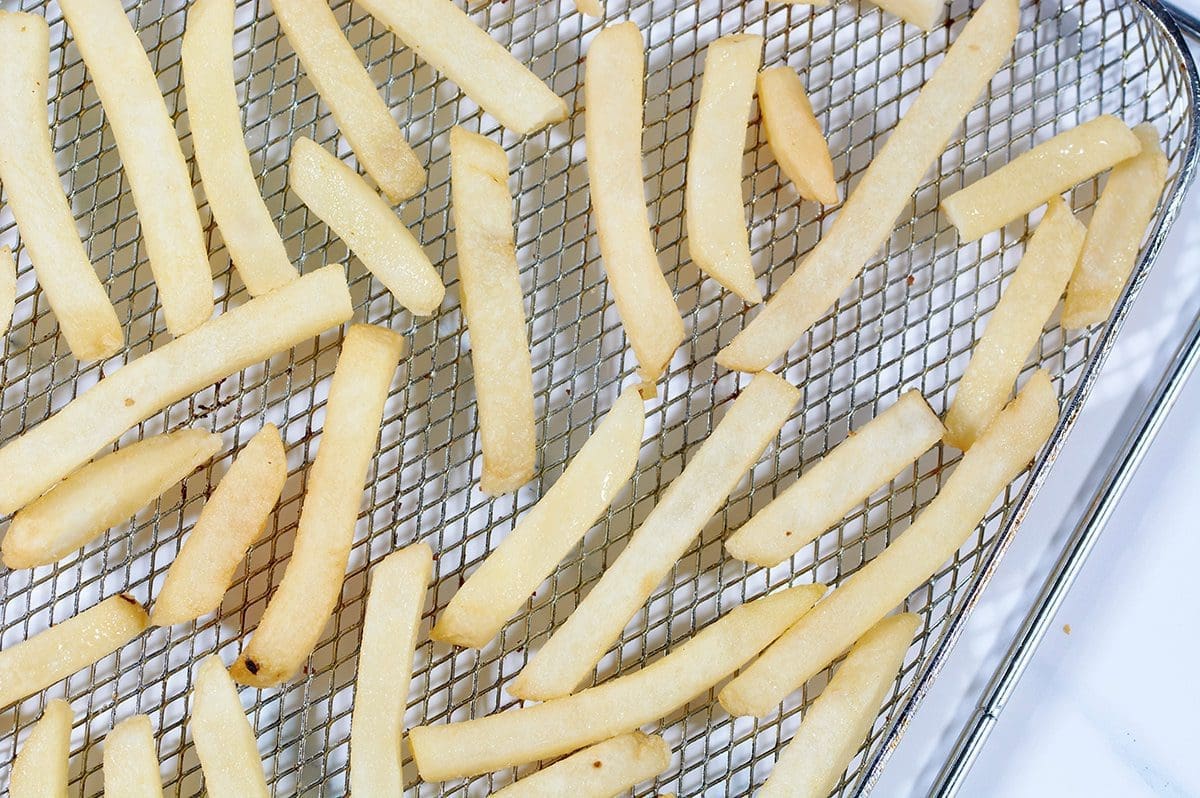 Frozen uncooked french fries on an air fryer tray.