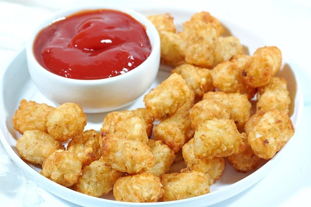 Crispy Air Fryer Tater Tots on a white plate next to a bowl of ketchup.