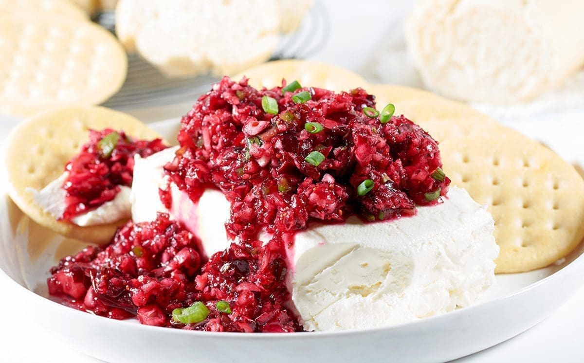 close up of cranberry jalapeno dip on a block of cream cheese surrounded by crackers