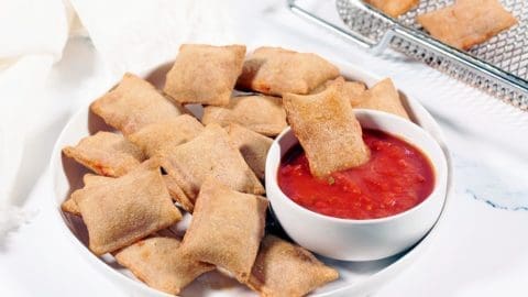 Air Fryer Pizza Rolls on a white plate with a bowl of marinara sauce. The air fryer basket is in the background.