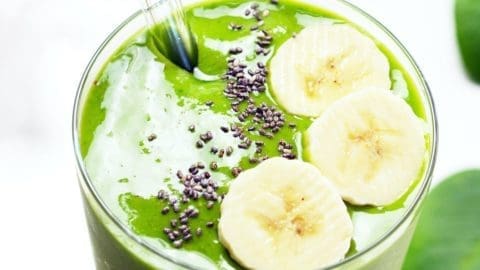 Healthy Green Smoothie in a short glass with a glass straw. Smoothie is topped with 3 banana slices and chia seeds.