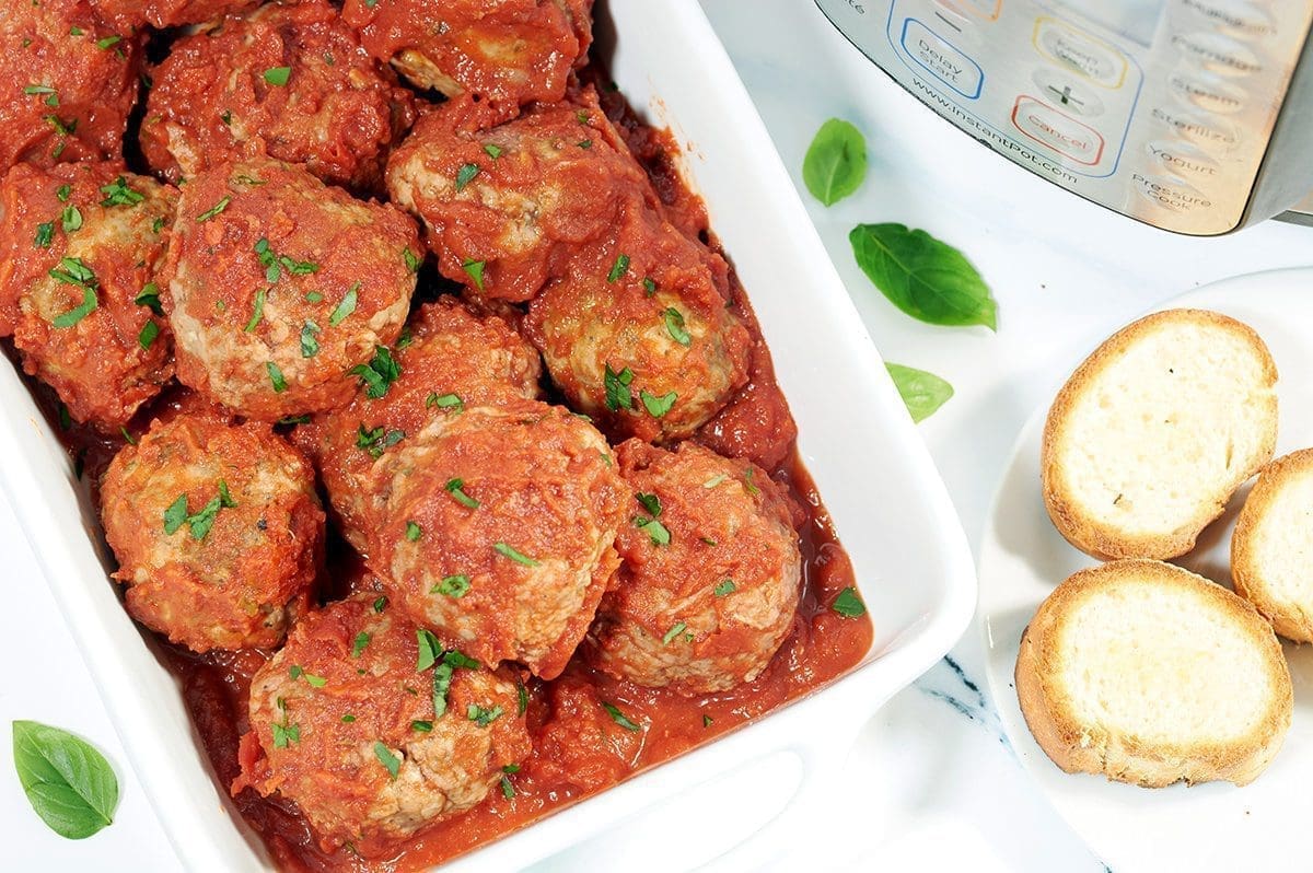 Cooked instant pot meatballs in a white casserole dish next to an instant pot and three slices of french bread.