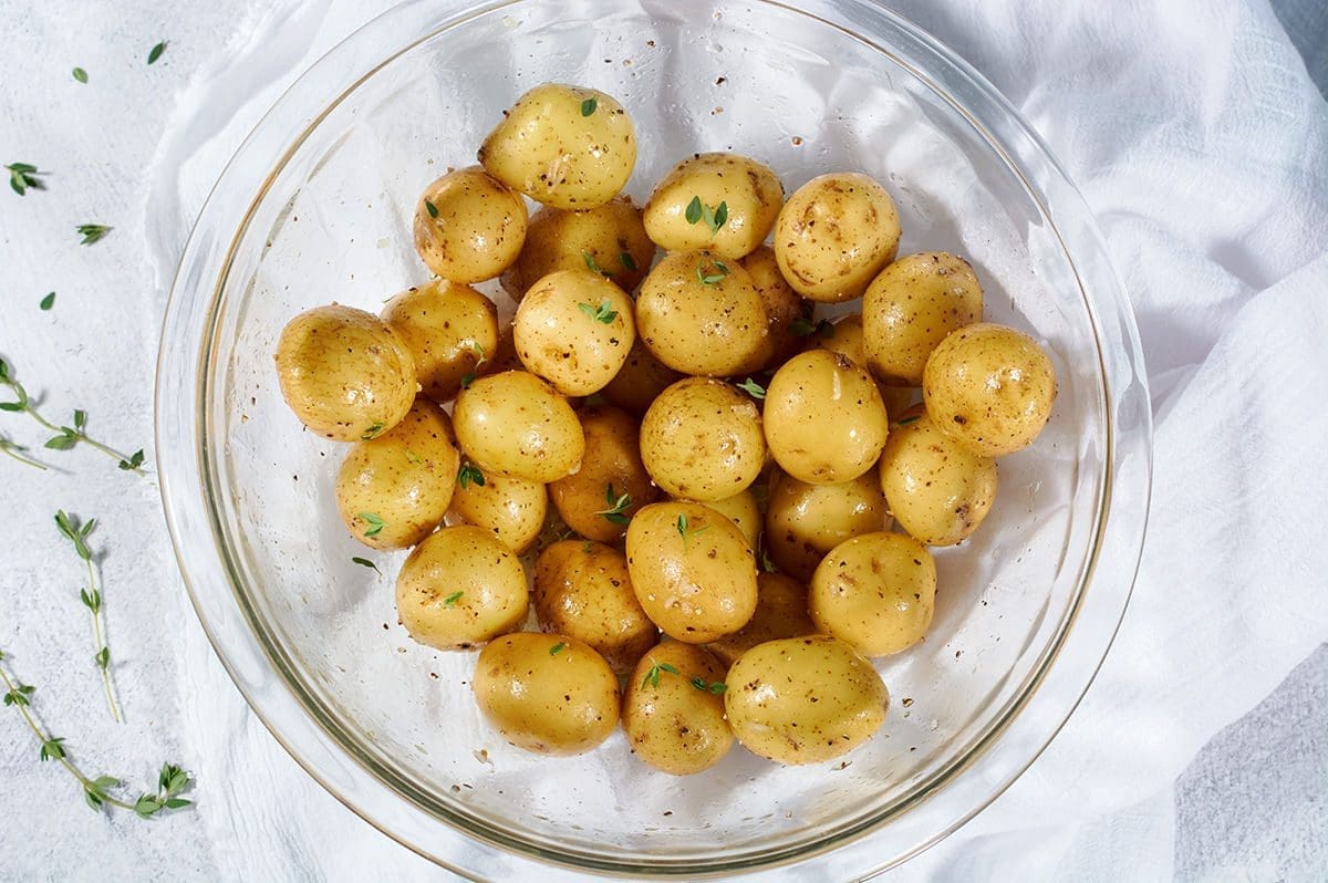 Overhead shot of uncooked baby potatoes, tossed with oil and spices, in a large clear mixing bowl.