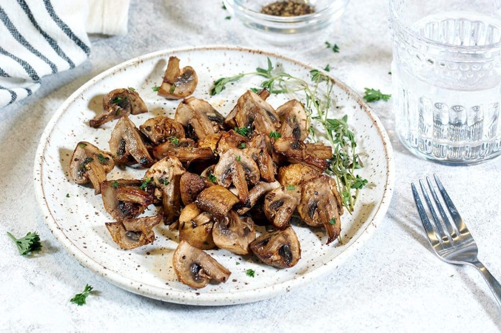 Air fryer mushrooms on spotted plates with thyme leaves. Next to the plate are water, forks and stripped blue napkins.