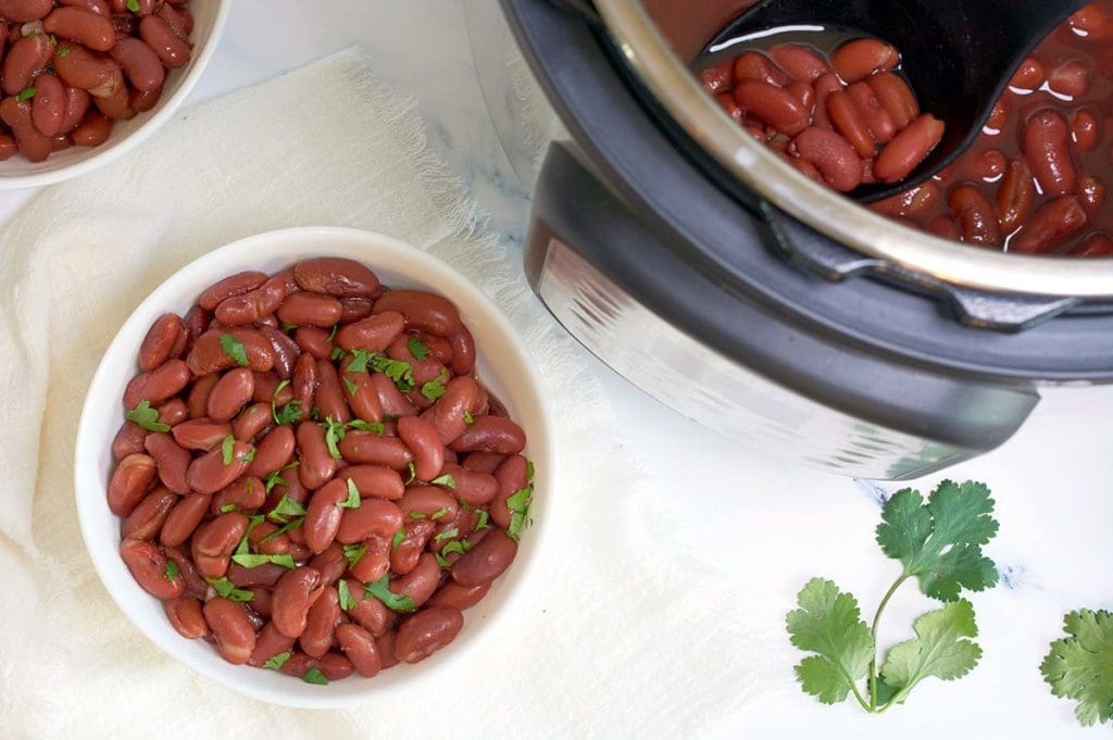 Instant Pot Kidney Beans in a white bowl, sitting next to the full Instant Pot full of beans.