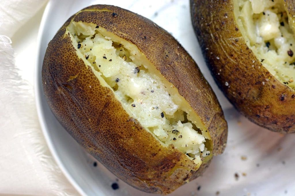 Close up of a cooked baked potato split open and covered with butter and salt.