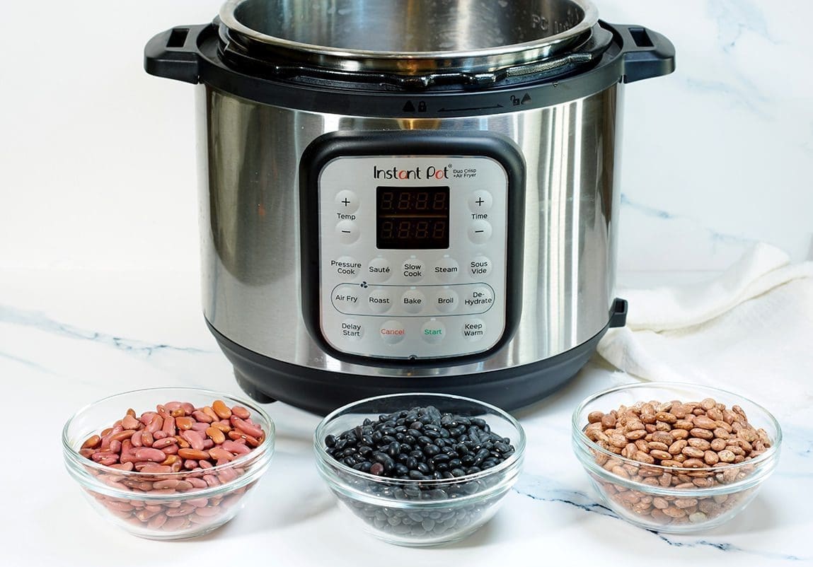 Three clear bowls of various uncooked beans with an instant pot in the background.