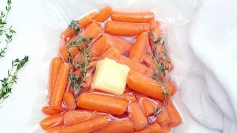 Close up of raw sous vide carrots in a sous vide bag filled with carrots, butter and thyme.