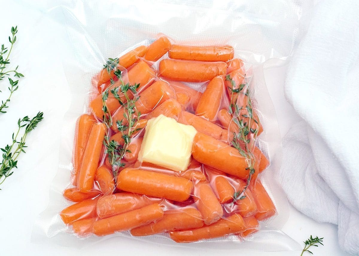 Close up of raw sous vide carrots in a sous vide bag filled with carrots, butter and thyme.