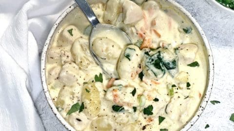 Close up photo of Olive Garden Chicken Gnocchi Soup in a ceramic bowl. A small white bowl of parsley and white napkin is also in the shot.