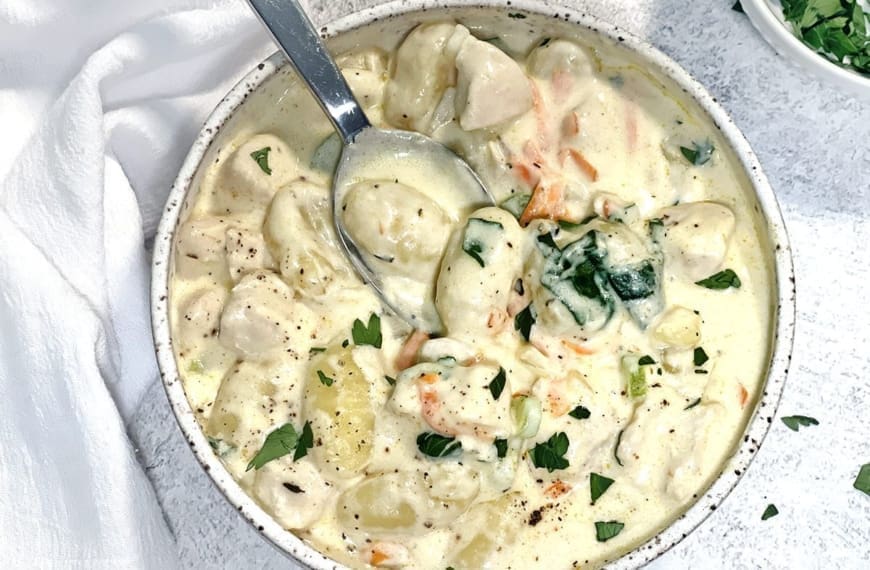 Close up photo of Olive Garden Chicken Gnocchi Soup in a ceramic bowl. A small white bowl of parsley and white napkin is also in the shot.