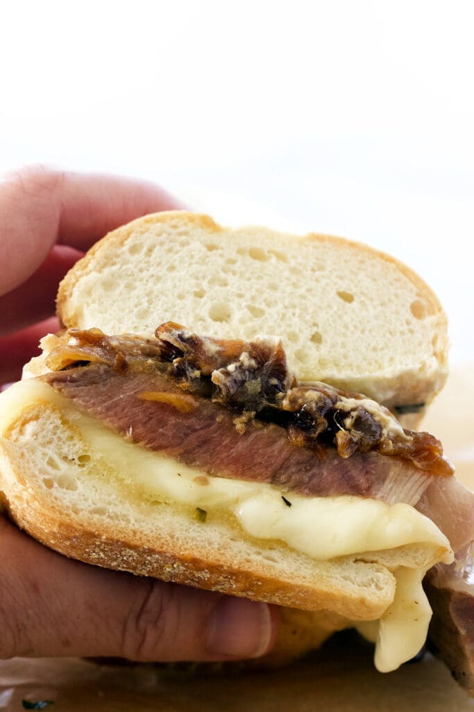 Hand holding prime rib sandwich cut in half.