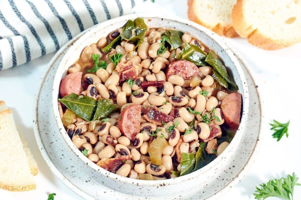 Overhead shot of a bowl of black eyed peas. Slices of bread and a striped napkin are nearby.