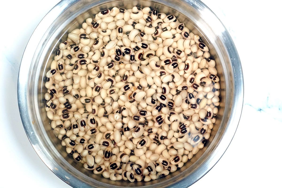 Uncooked black eyed peas soaking in a silver bath of water.