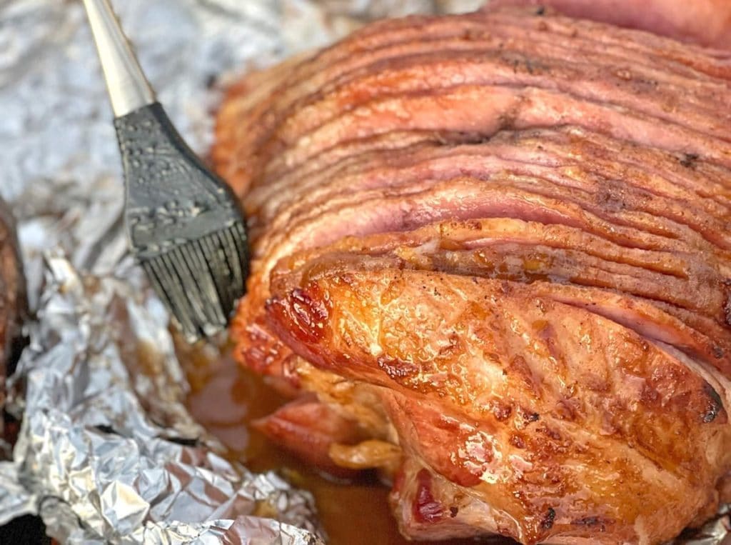 Close up of a smoked ham with a silicone brush basting it with glaze.