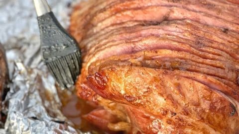 Close up of a smoked ham with a silicone brush basting it with glaze.