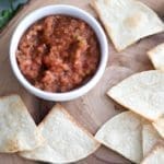 Air Fryer Tortilla Chips on a wooden plate next to a small white bowl of salsa.