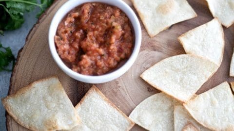 Air Fryer Tortilla Chips on a wooden plate next to a small white bowl of salsa.