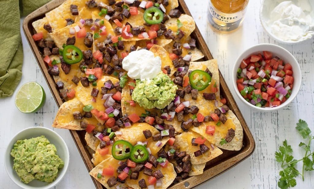 Caan Asada Nachos on a baking sheet surrounded by bowls of guacamole, pico de gallo and sour cream.