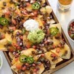 Carne Asada nachos on a baking sheet surrounded by bowls of guacamole, pico de gallo and sour cream.