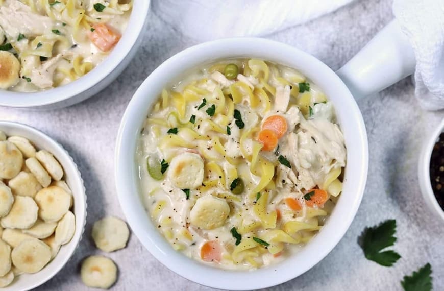 Creamy chicken noodle soup in a white bowl.