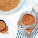 Small clear jar of seasonings on a metal mesh plate. A white bowl of the same seasoning is next to it.