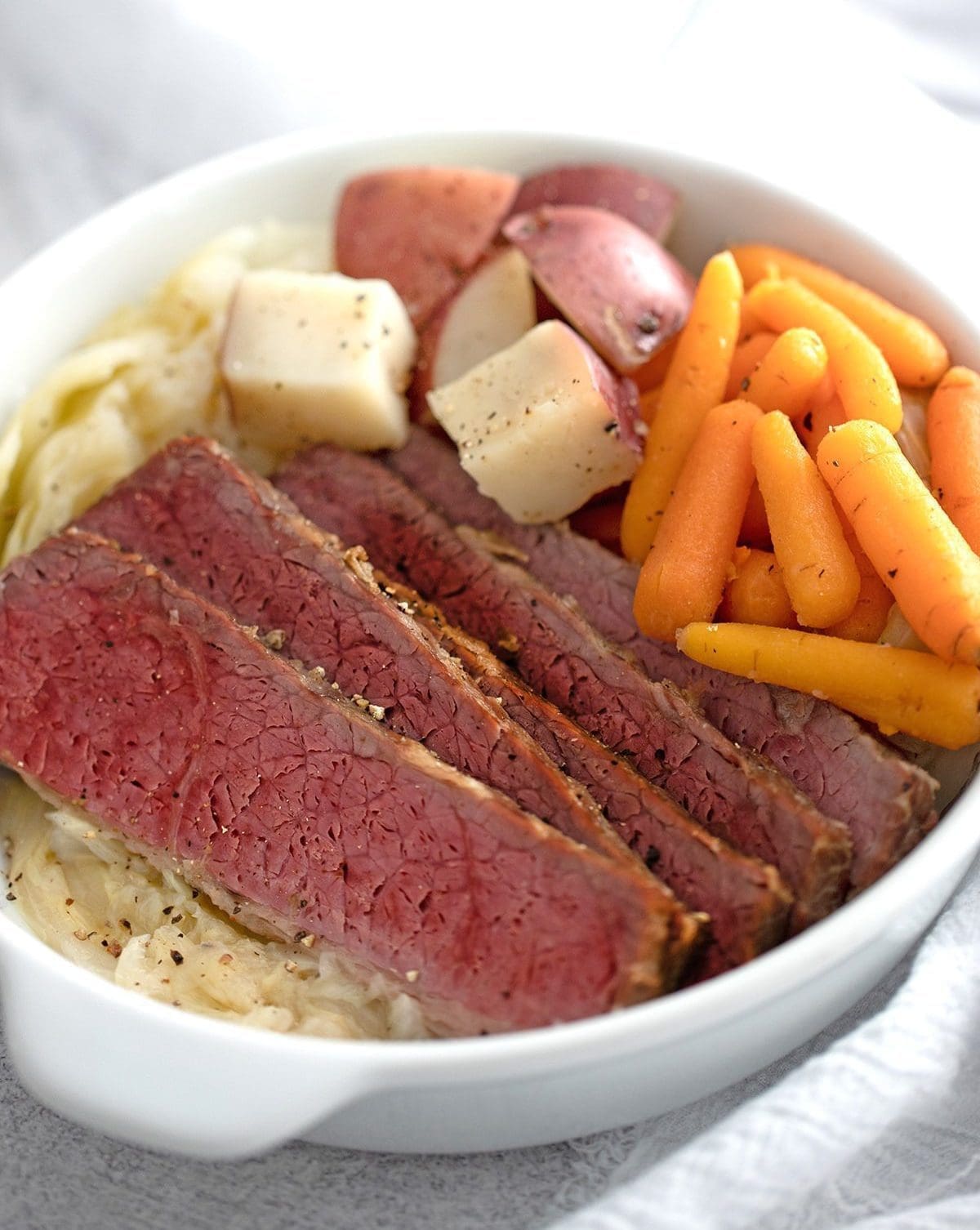 Instant Pot Corned Beef, carrots, cabbage and potatoes in a white bowl.