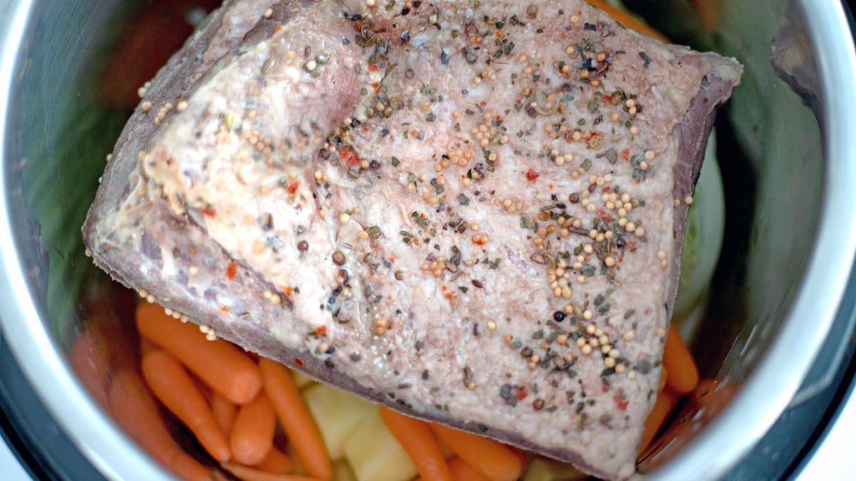 Close up of corned beef set upon carrots and potatoes.