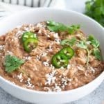 Instant Pot Refried Beans in a white bowl topped with cheese, jalapenos and cilanto.