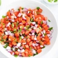 Pico de gallo in a white bowl surrounded by individual ingredients.