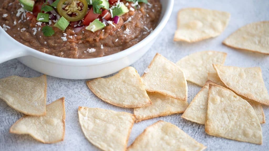 Next to a bowl of air fryer corn tortilla chips chips lift raveen dip.