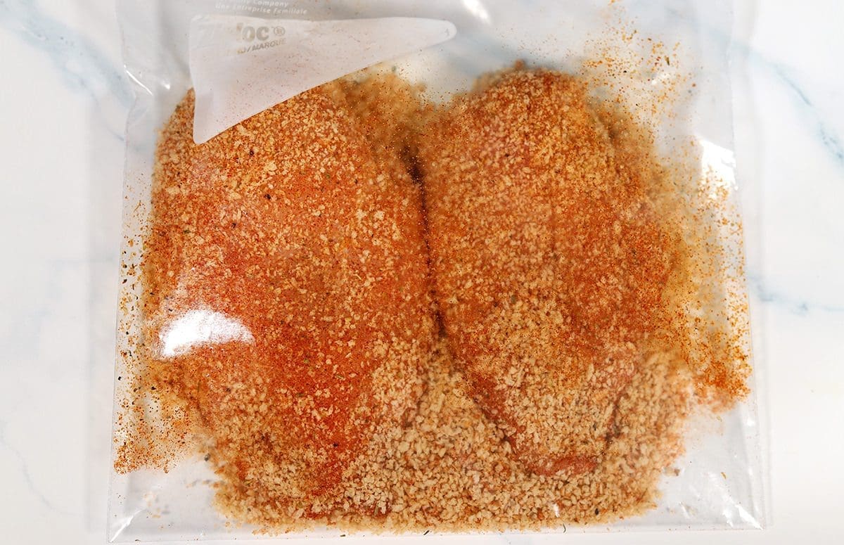 Two raw chicken breasts in a ziploc bag full of shake and bake.