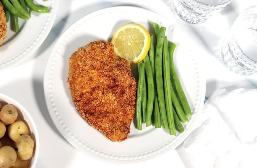 Shake and Bake Chicken on a white plate with a slice of lemon and green beans.